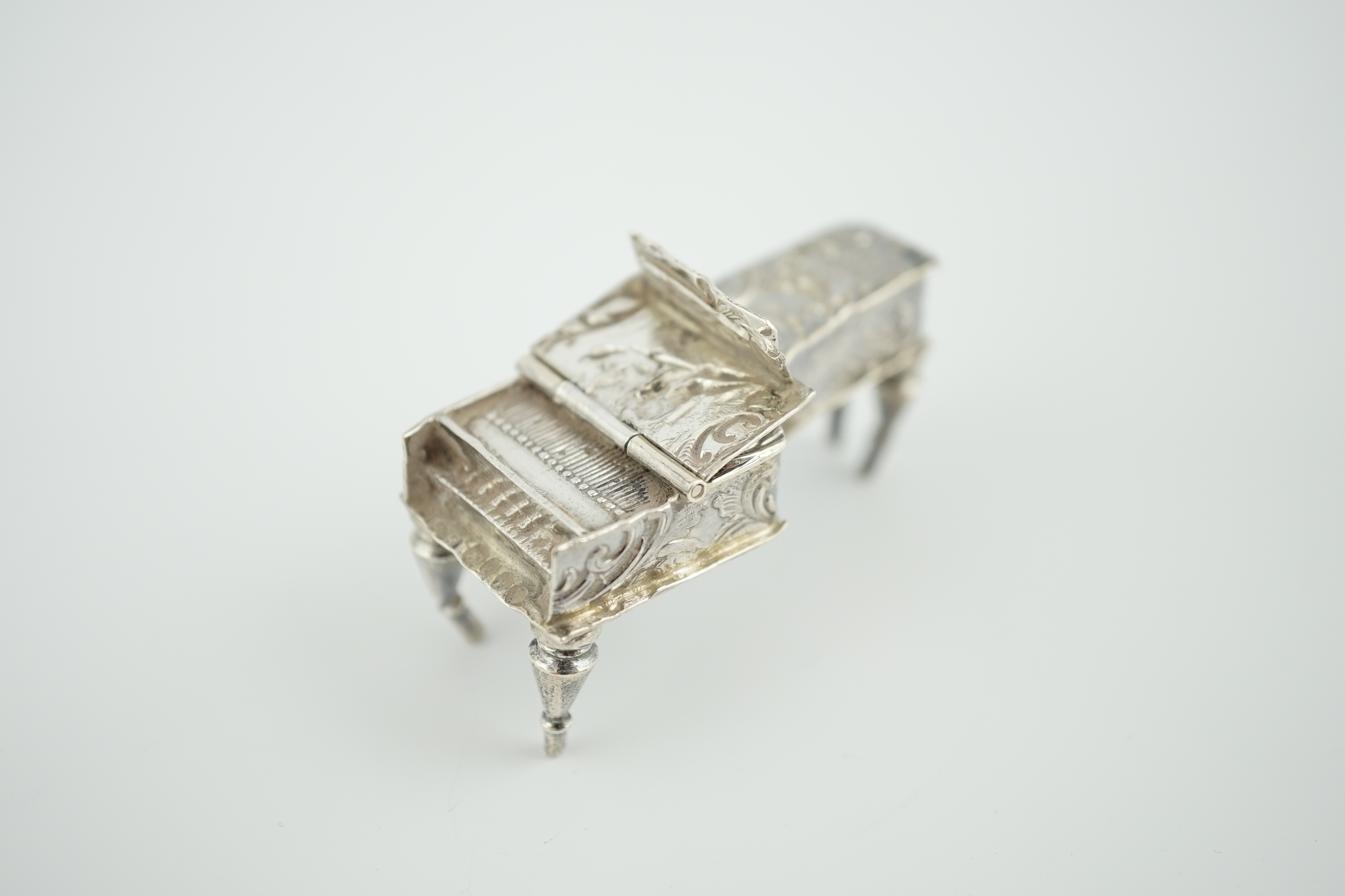 A late 19th century continental embossed silver miniature model of grand piano, length 53mm, together with a similar model of a table/desk on ornate scroll supports